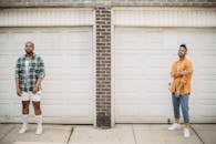 Man in Blue Denim Jeans and White Sneakers Standing in Front of White Wooden Door