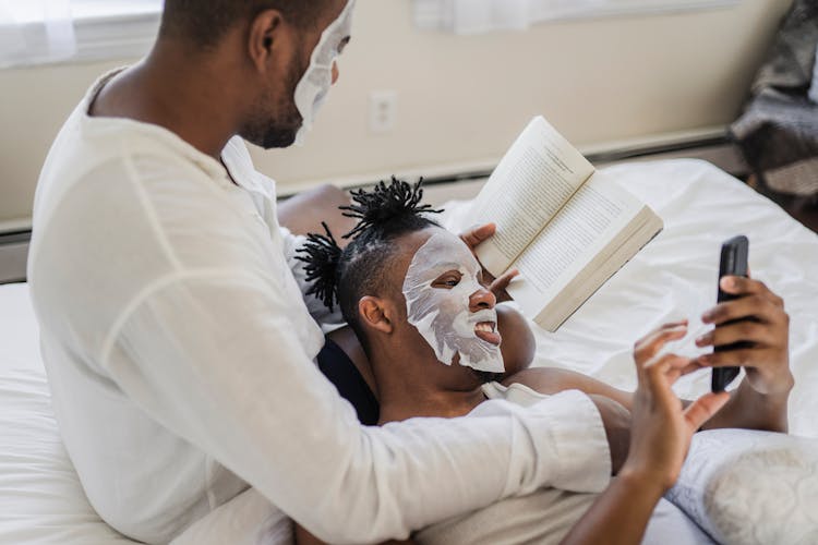 A Couple Doing Their Own Stuffs While Staying On Bed