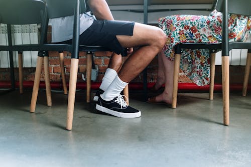 Person in Black Shorts and White Nike Sneakers Sitting on Brown Wooden Chair