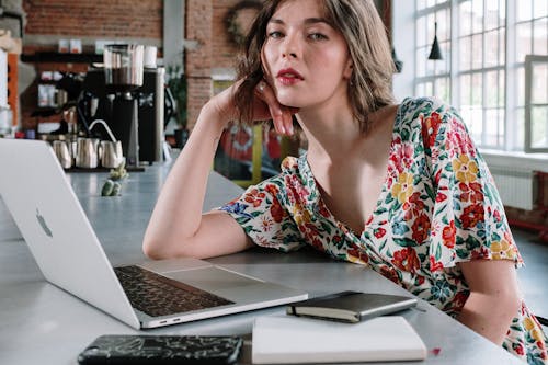 Mulher Em Uma Camisa Sem Mangas Floral Vermelha E Azul Branca Sentada à Mesa Usando Um Macbook