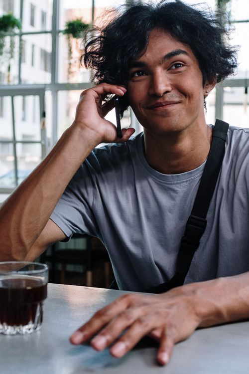 Free Smiling young man with curly hair using smartphone in a trendy café. Stock Photo