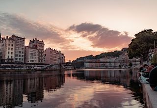 Beautiful sunset view over the Saone River in Lyon, France, showcasing urban townhouses and reflections.