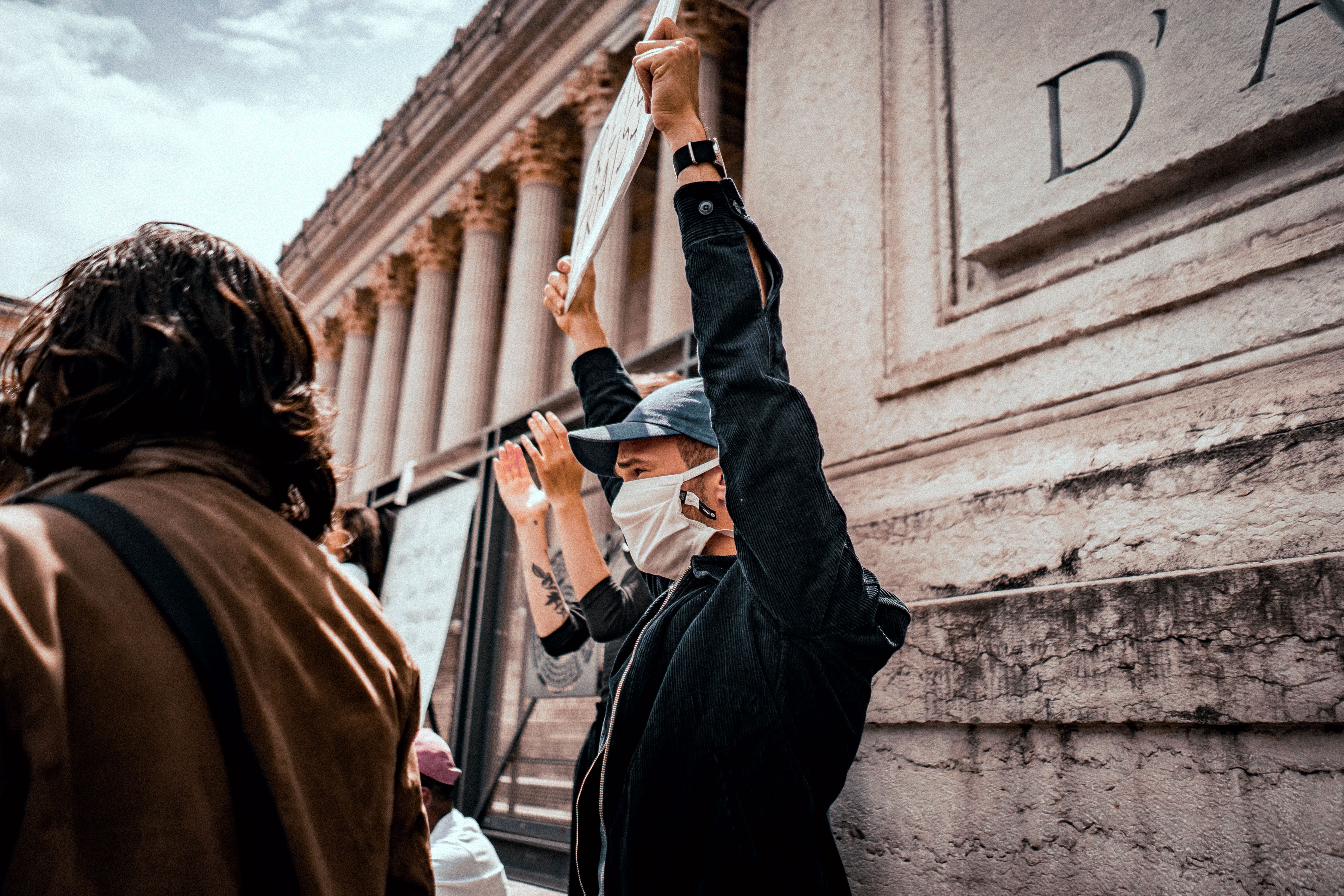Masked protesters demonstrating in Lyon, France, with placards expressing social justice themes.