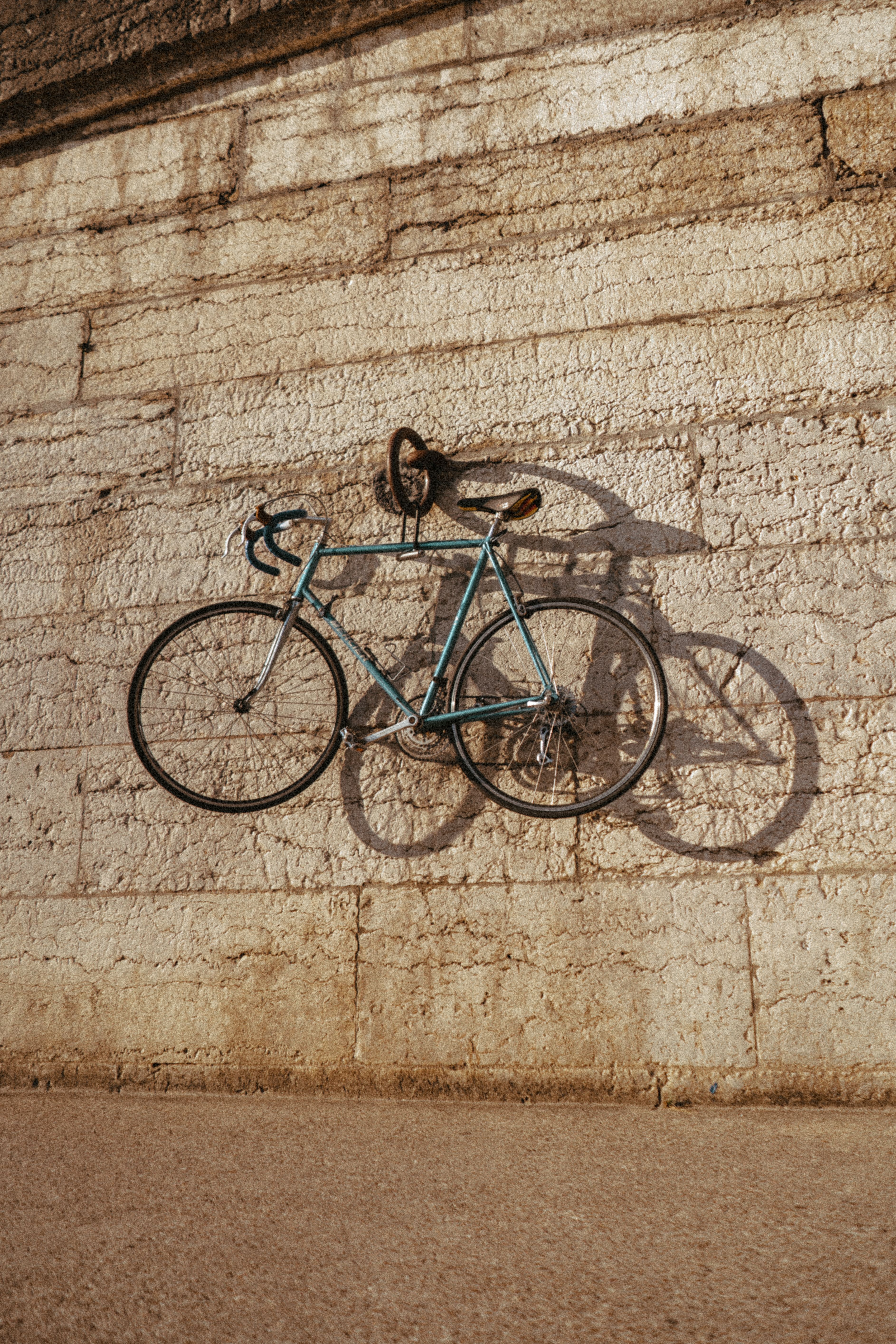 A vintage bicycle hangs on a stone wall, casting a shadow in Lyon.