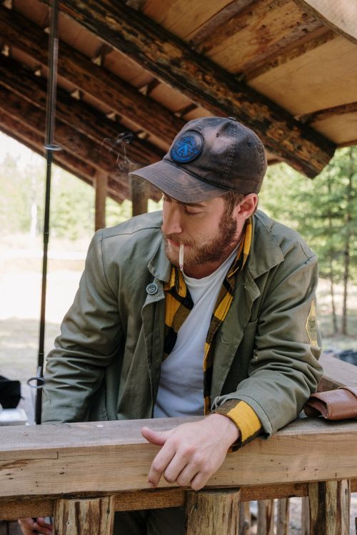 Free Man enjoying a moment by a wooden house, outdoors, holding a fishing rod. Stock Photo