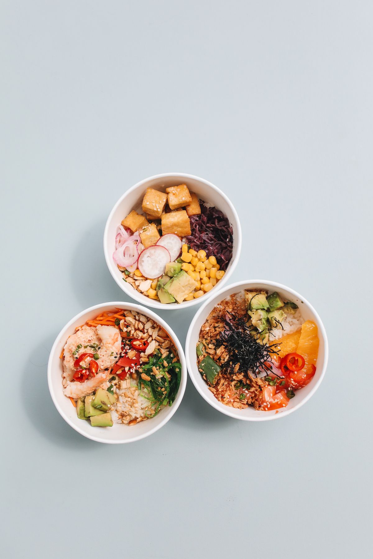 Colourful nourish bowls filled with vegetables, grains and protein on a teal background, a balanced approach to eating for fat loss