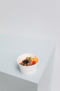 Minimalist poke bowl with fresh toppings on a pastel surface, creating a modern and clean aesthetic.