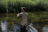 一个人在宁静的河边钓鱼，四周绿树环绕