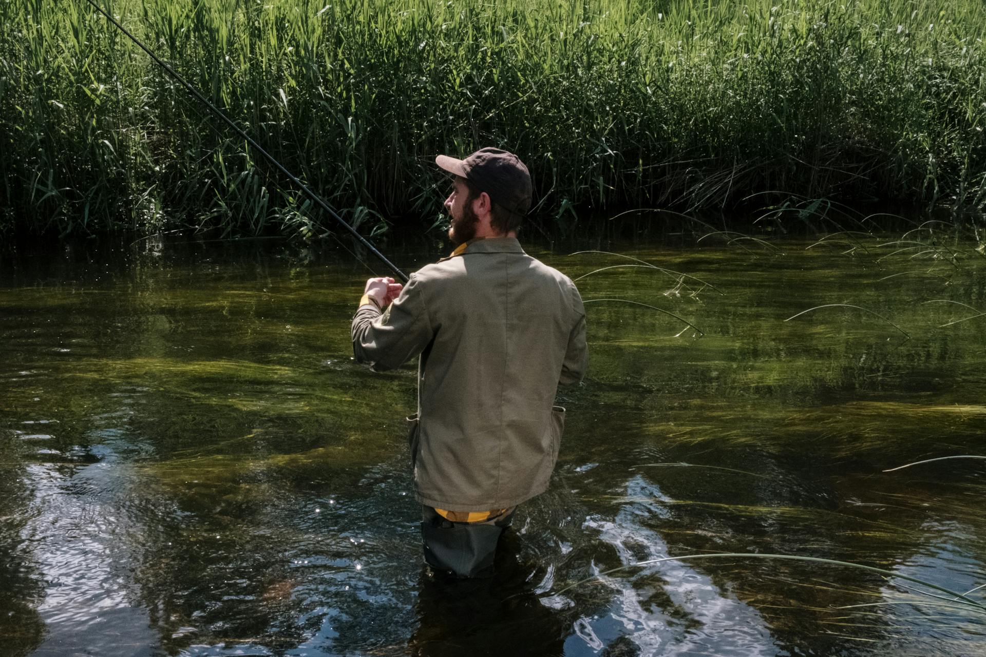 Man in Gray Sweater and Black Shorts Fishing on River