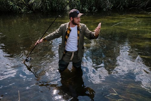 Man in Brown Jacket and Black Pants Fishing on River