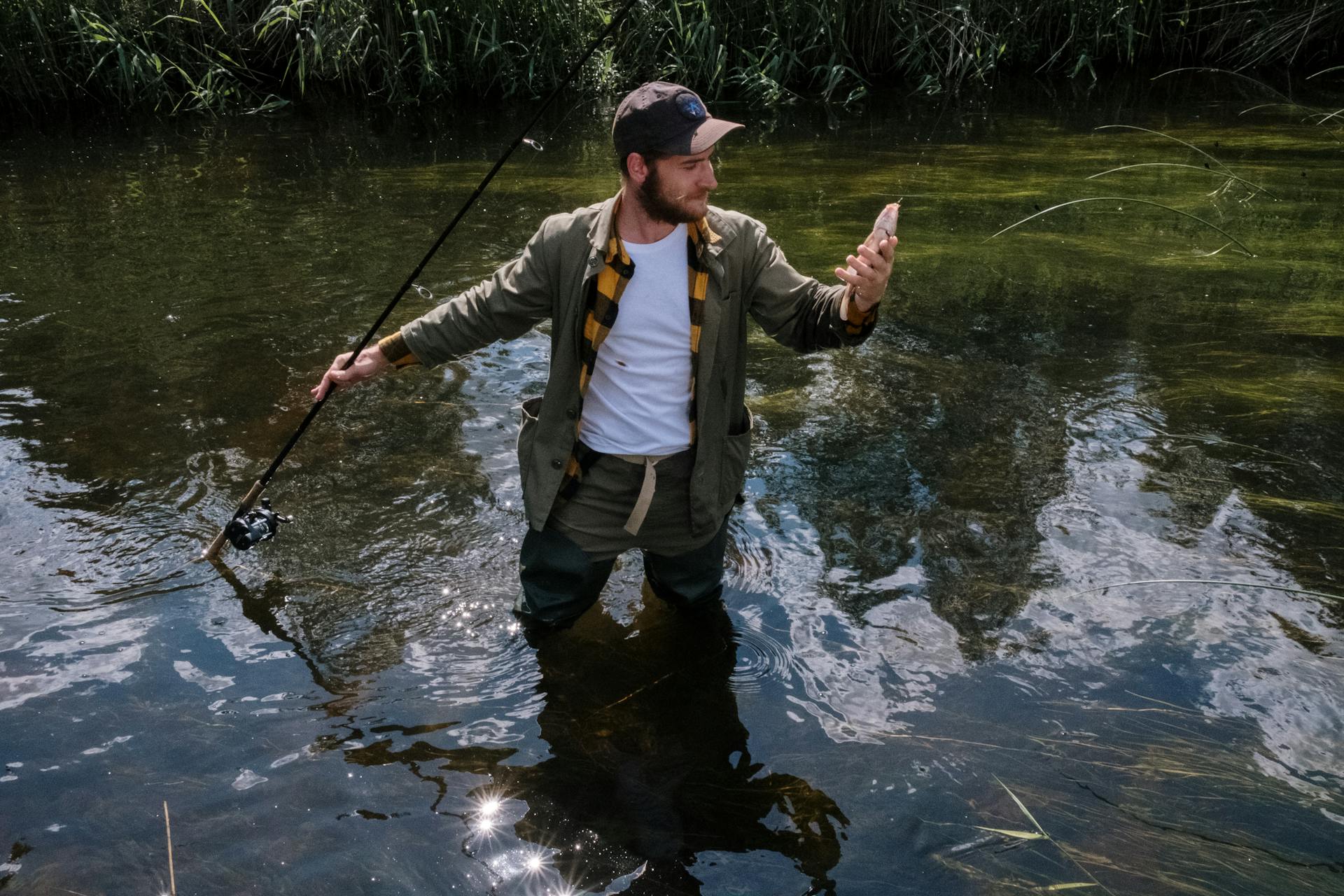 Man in Brown Jacket and Black Pants Fishing on River