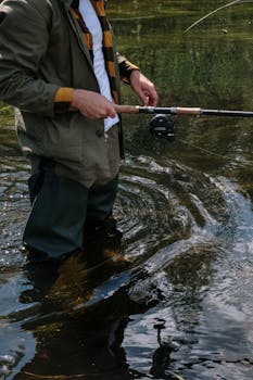 A man in waders fly fishing in a river during daytime.