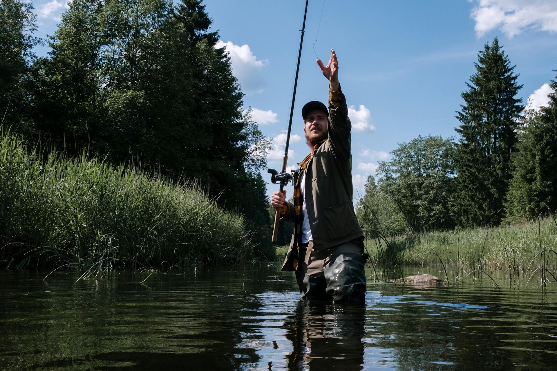 Man in Blue Shirt and Black Pants Fishing on River