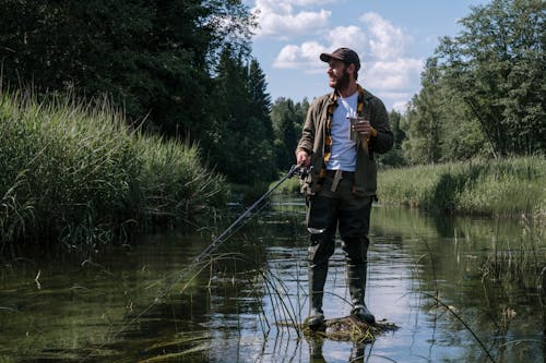 Man in Blue Jacket and Blue Denim Jeans Standing on Brown Log on River