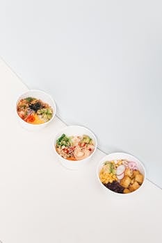 Three delicious poke bowls filled with vibrant and fresh ingredients in white bowls on a white surface.