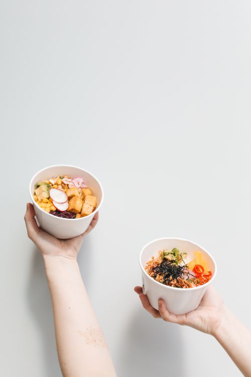 Free Fresh and healthy poke bowls featuring tofu and vegetables held by hands against a white backdrop. Stock Photo