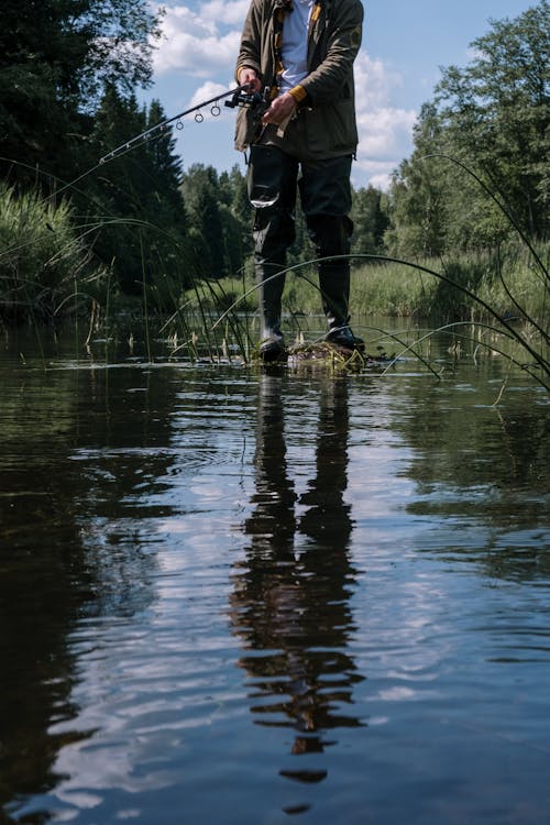 Man in Black Jacket and Black Pants Standing on Brown Log on River