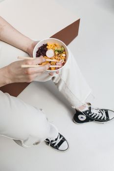 Overhead shot of hands holding a vibrant poke bowl with chopsticks.