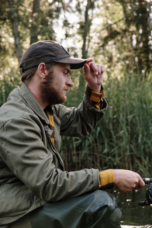 Free A man in casual attire fishing at a serene countryside location, surrounded by reeds. Stock Photo