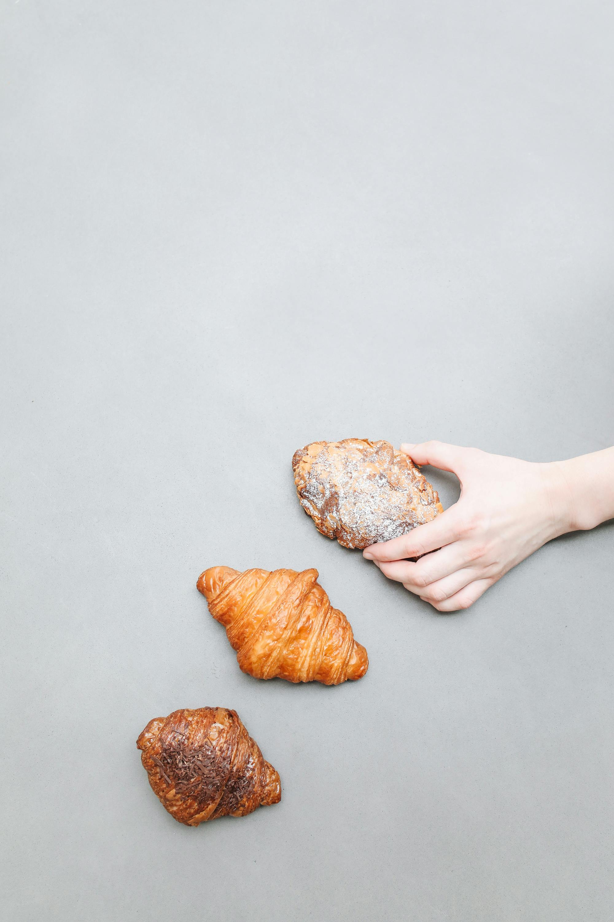 Hand picking fresh pastries from a minimalist gray surface for a food-themed composition.