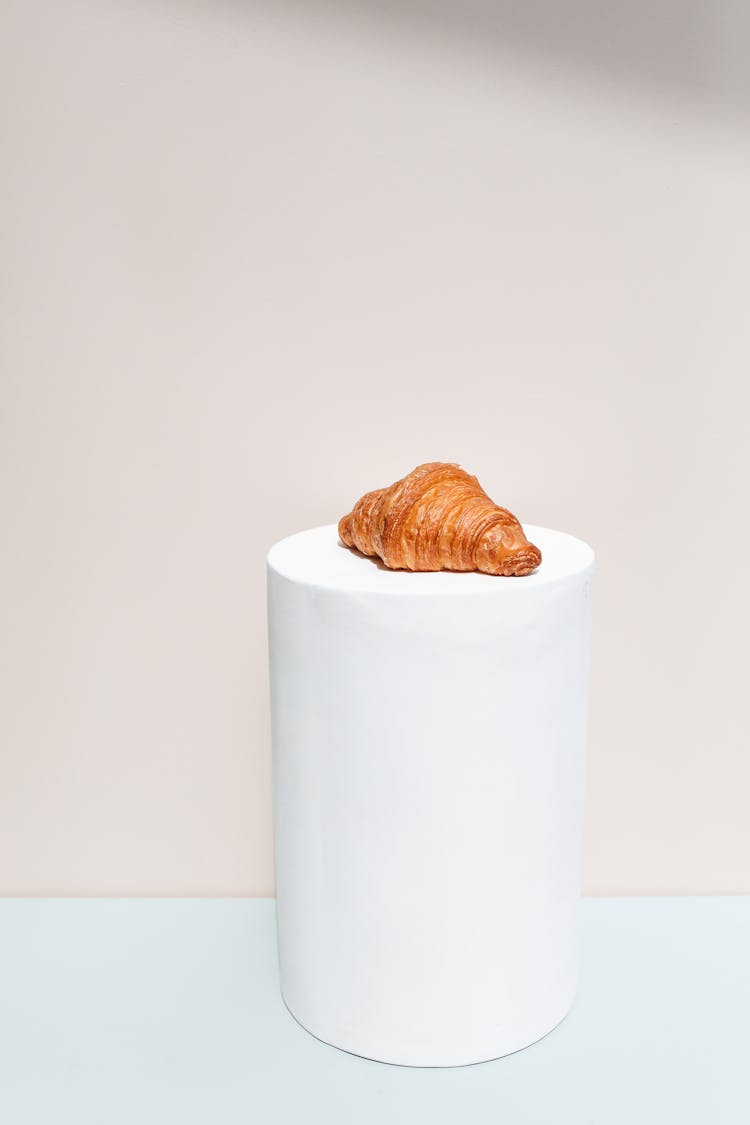 Photograph Of A Croissant On A White Cylinder