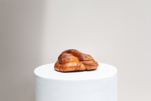 A single cardamom knot bun elegantly presented on a minimalist white pedestal against a neutral background.