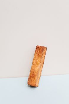 垂直镜头下，一个金色酥脆、如法式面包般的糕点置于柔软背景之中