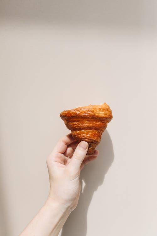 Free Photograph of a Person's Hand Holding Half of a Croissant Stock Photo