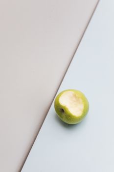 Minimalist photo of a green apple with a bite, placed on a pastel background, creating a modern aesthetic.