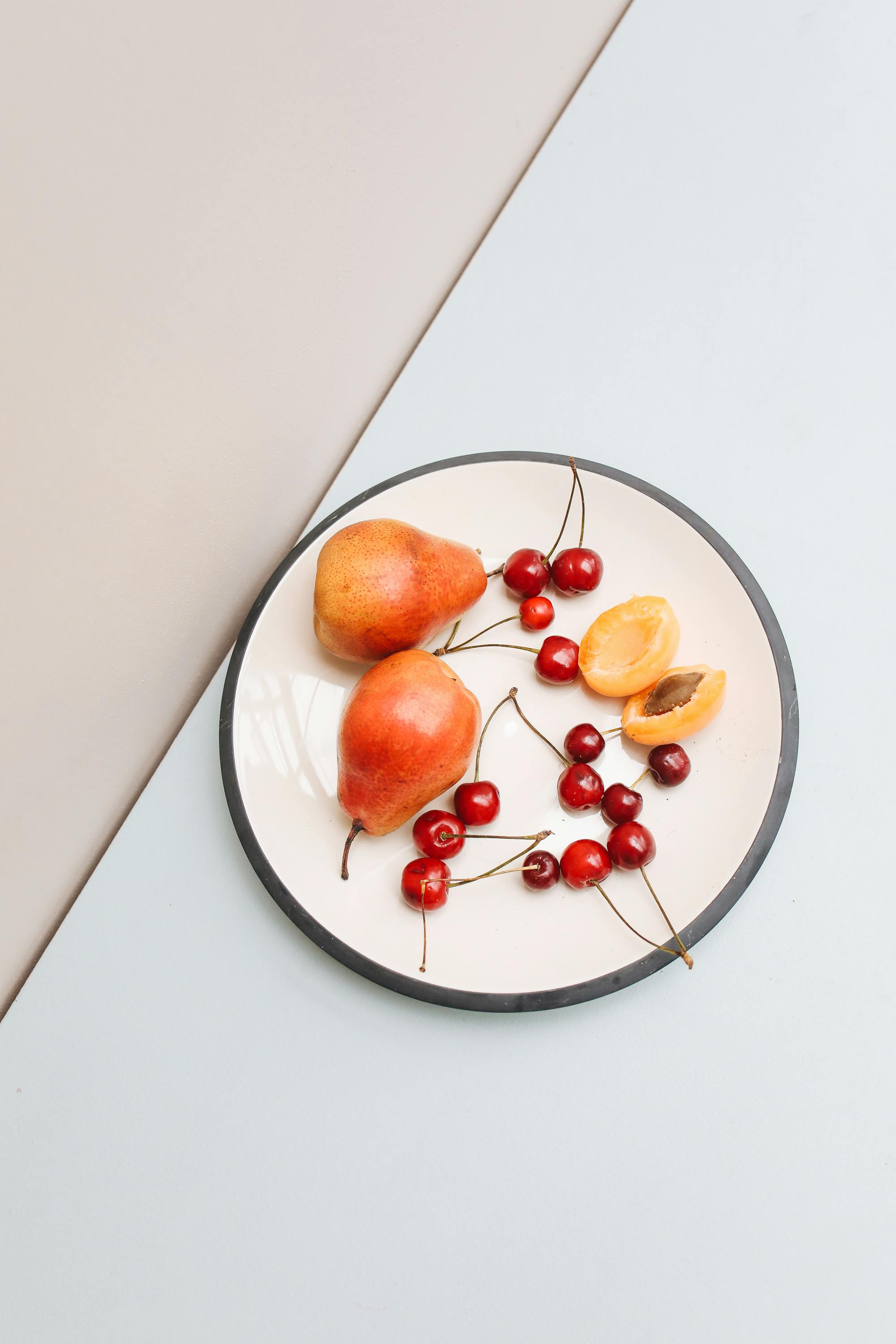 A vibrant display of pears, cherries, and apricot on a ceramic plate. Perfect for food photography.