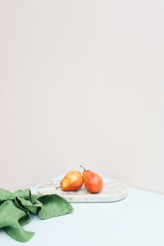 简约的构图中，两个充满活力的梨置于大理石板上，背景柔和