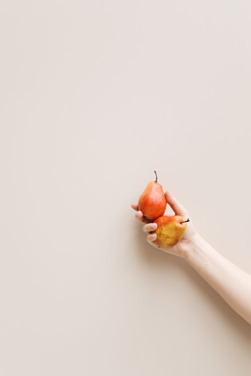 Free A minimalist photo of a hand holding two pears against a neutral background. Stock Photo