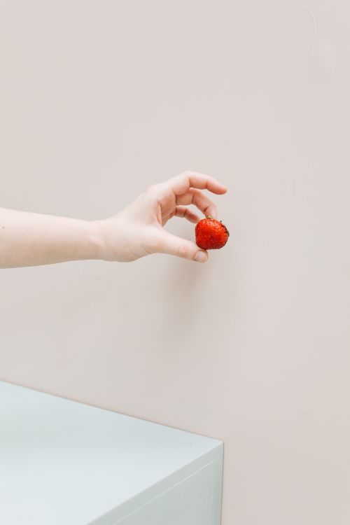 Free Minimalist image of a hand holding a fresh strawberry against a beige background. Stock Photo