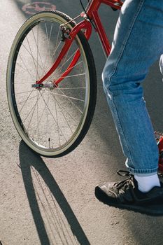一名男子穿着牛仔牛仔裤，在户外道路上骑着红色自行车，路面上有阴影