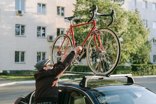 Free Person in Brown Jacket Putting His Red Bicycle on Top of the Car Roof  Stock Photo