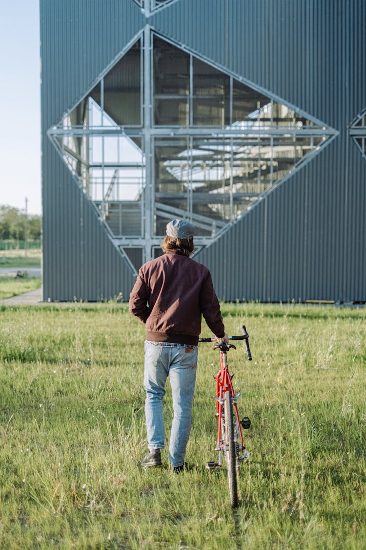 Back View Of A Man Walking Beside His Red Road Bike