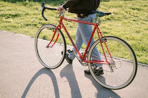 Person Walking on the Road While Holding the Red Bicycle