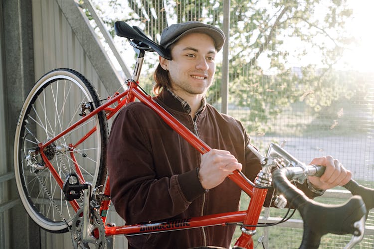 Photo Of A Man Carrying His Red Bike While Smiling