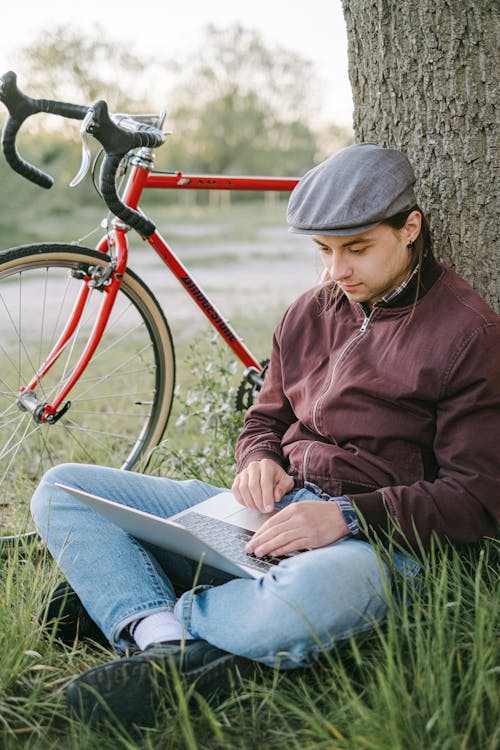 Free Man Sitting Under a Tree and Working on His Laptop Stock Photo