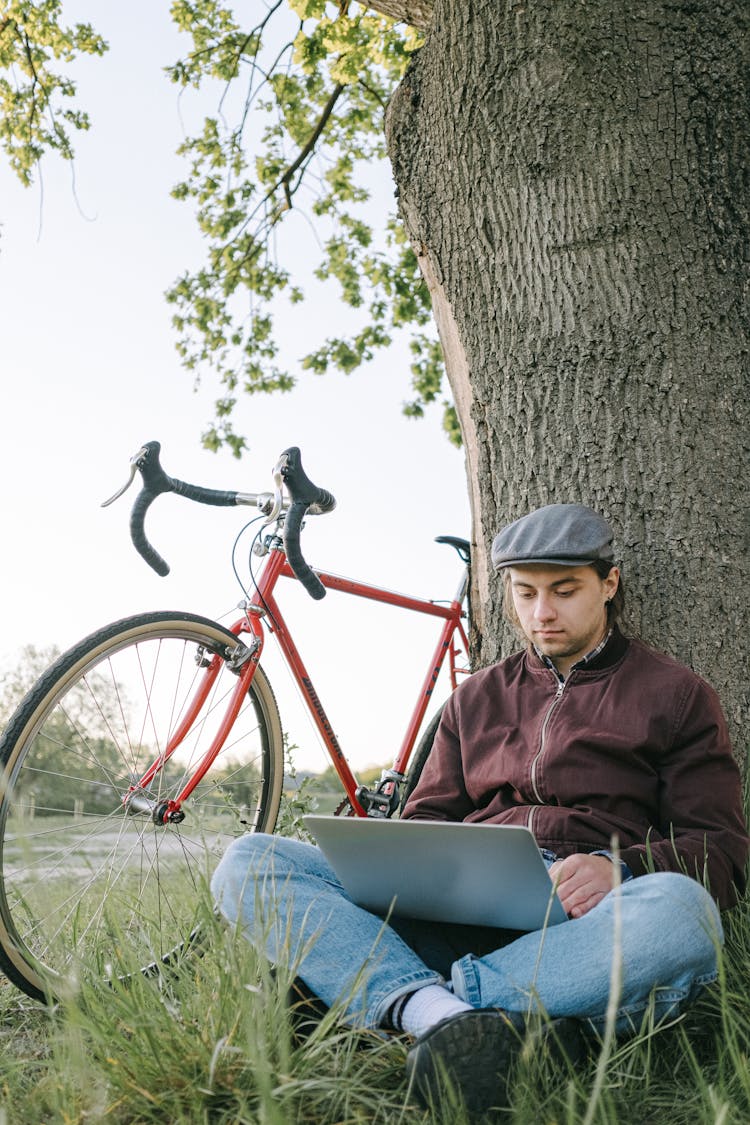 A Man Using A Laptop While Sitting Under A Tree