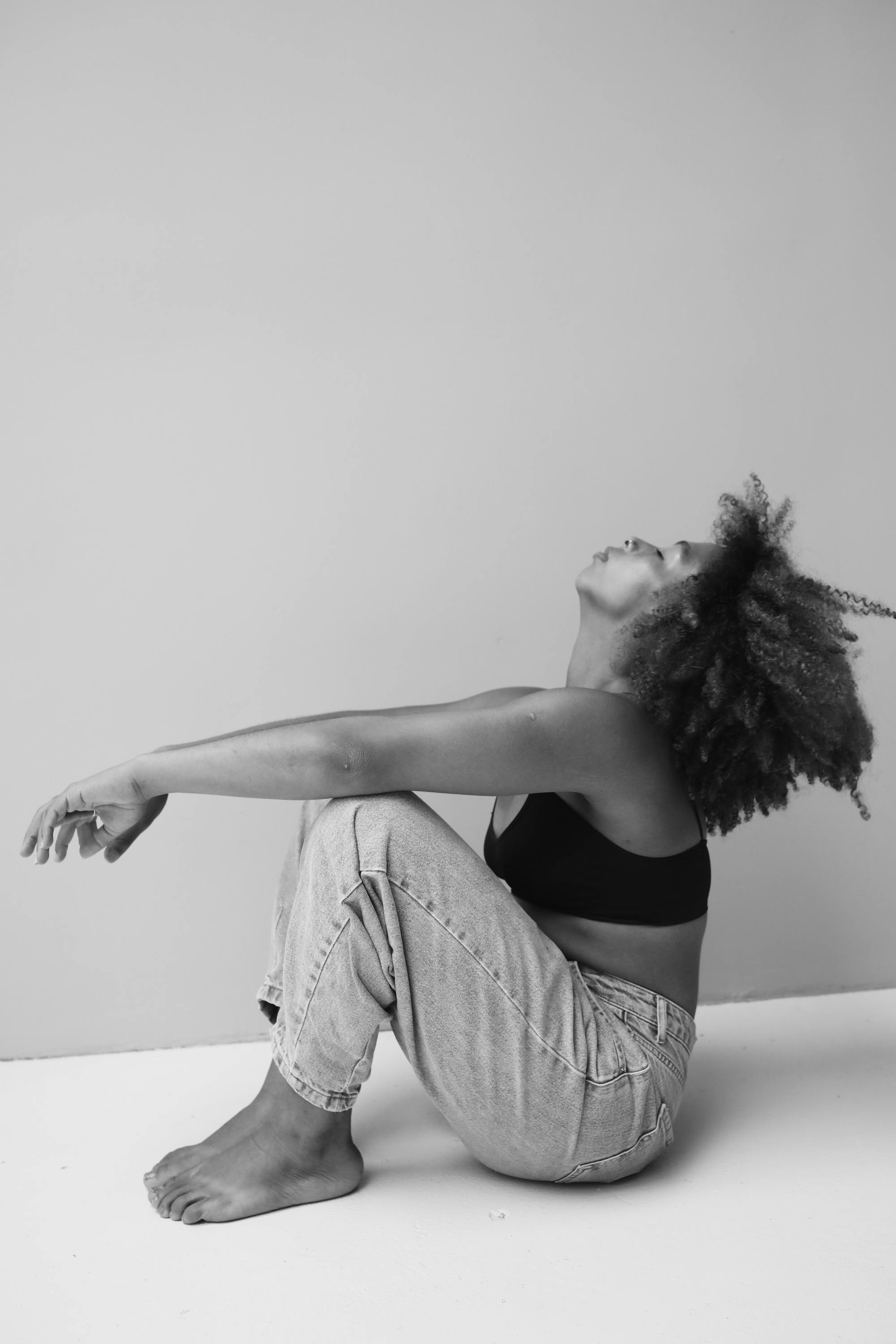 A black and white portrait of a woman with curly hair sitting relaxed against a wall.