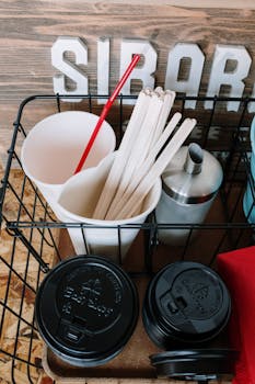 A collection of disposable coffee supplies inside a rustic café, featuring cups, lids, and stirrers.
