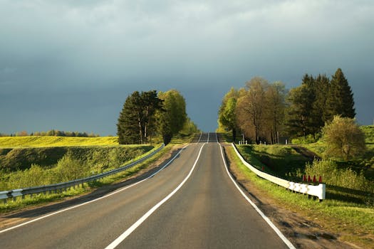 Empty country road winding through lush greenery under a cloudy sky, perfect for travel inspiration.