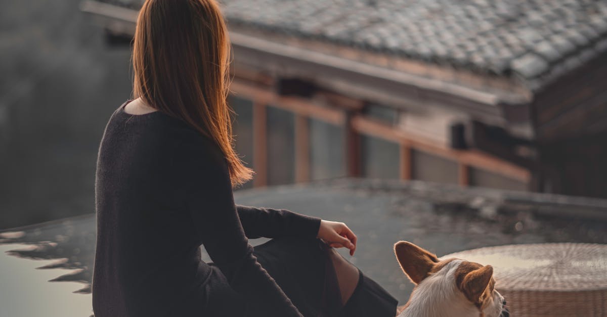 Faceless woman sitting against rural house and stroking cute Corgi
