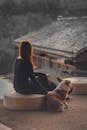 Faceless woman sitting against rural house and stroking cute Corgi