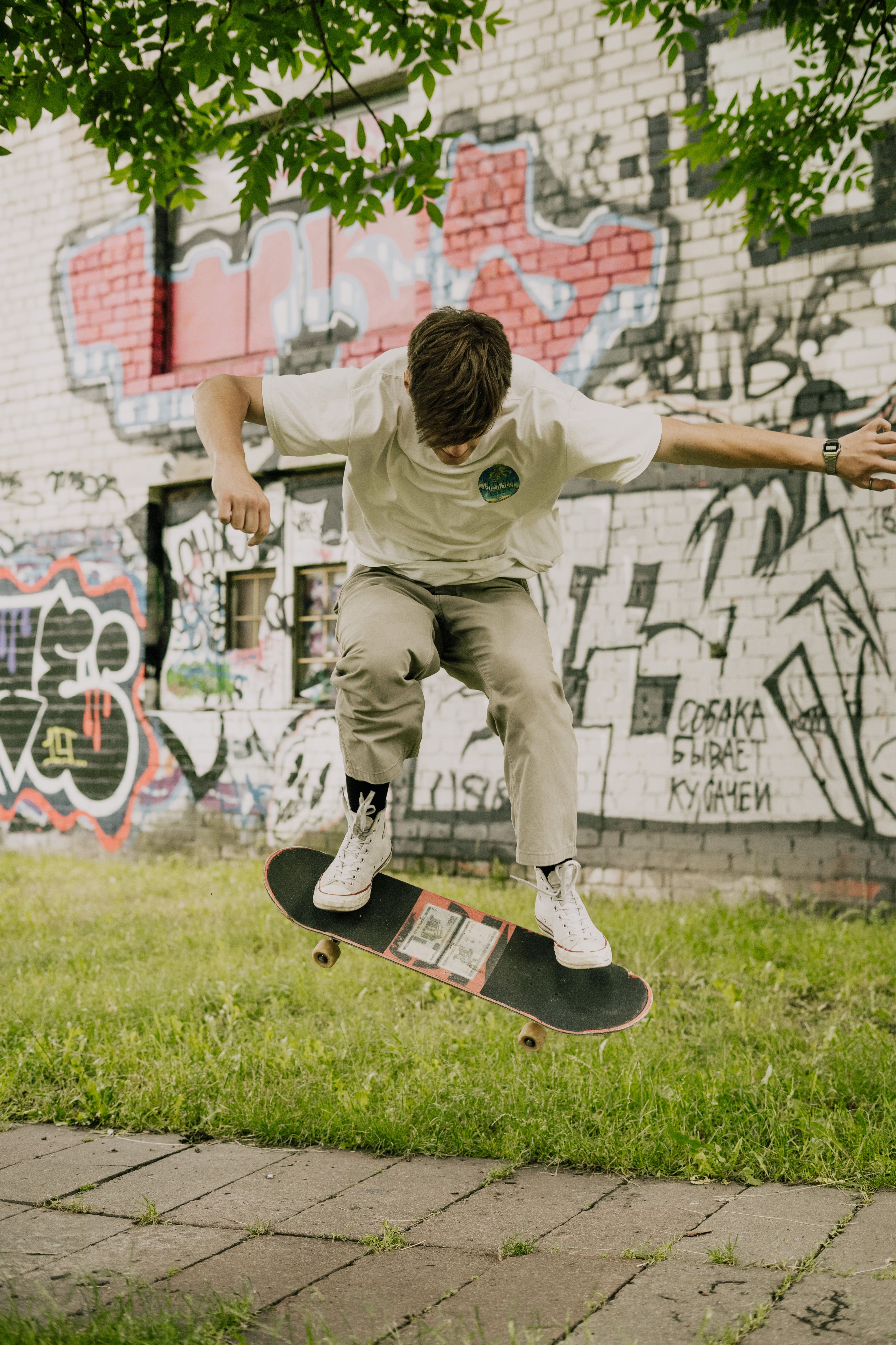 Teen skateboarder executing an ollie trick in graffiti-decorated urban park setting.