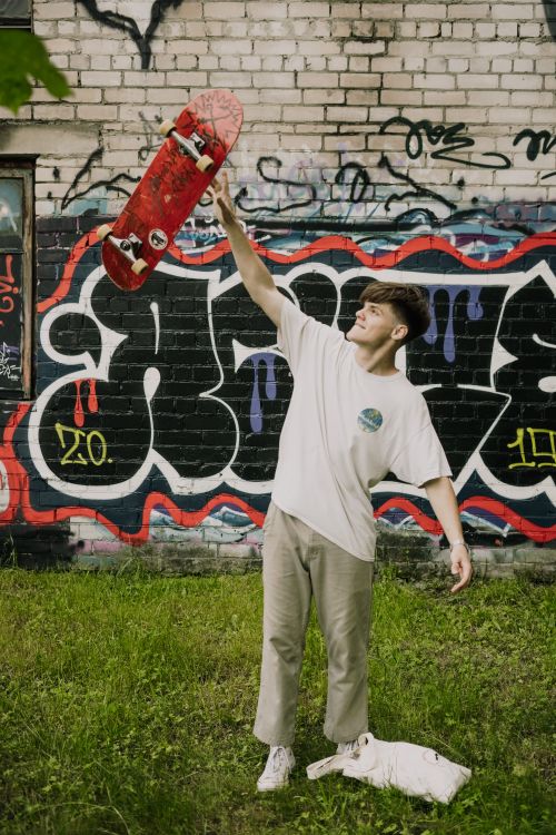 Free A young man holds his skateboard triumphantly in front of a vibrant graffiti wall, exuding confidence and creativity. Stock Photo