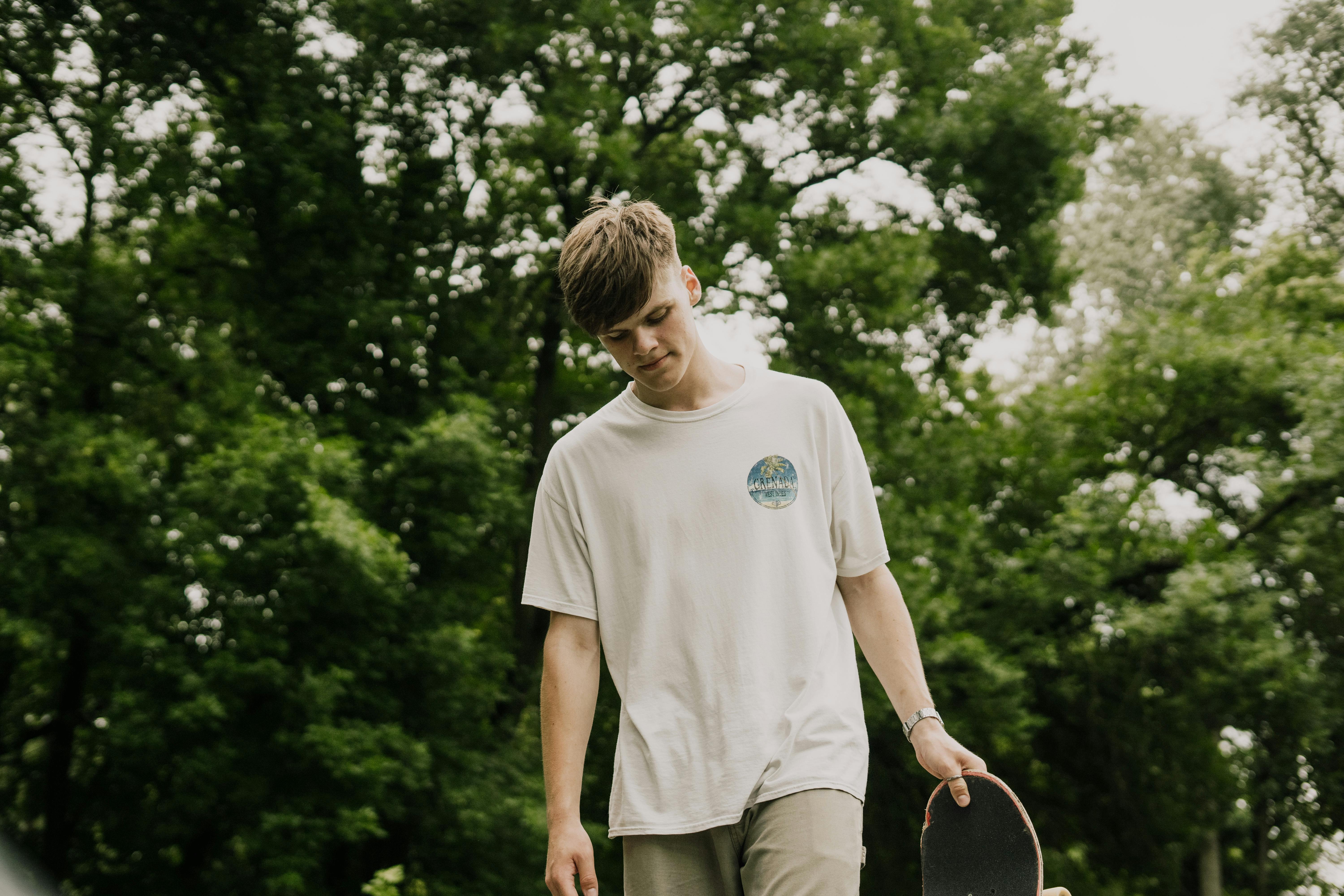 年轻人站在绿色公园的滑板上沉思