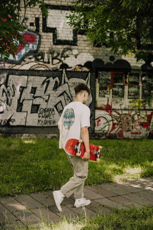 A Man Walking in a Park while Carrying a Skateboard