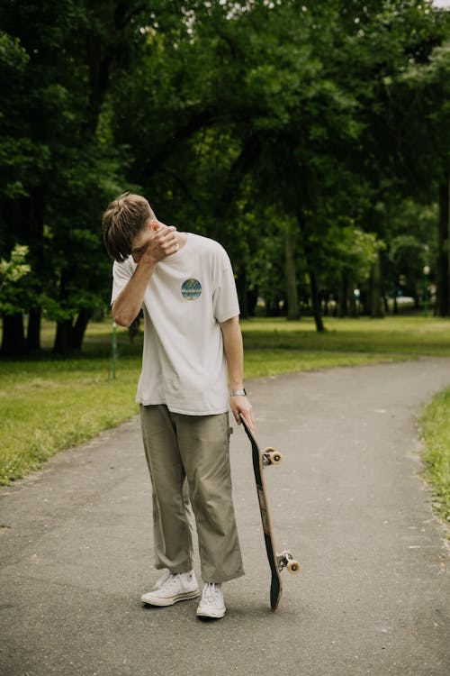 A Young Man Holding a Skateboard while standing in a Park